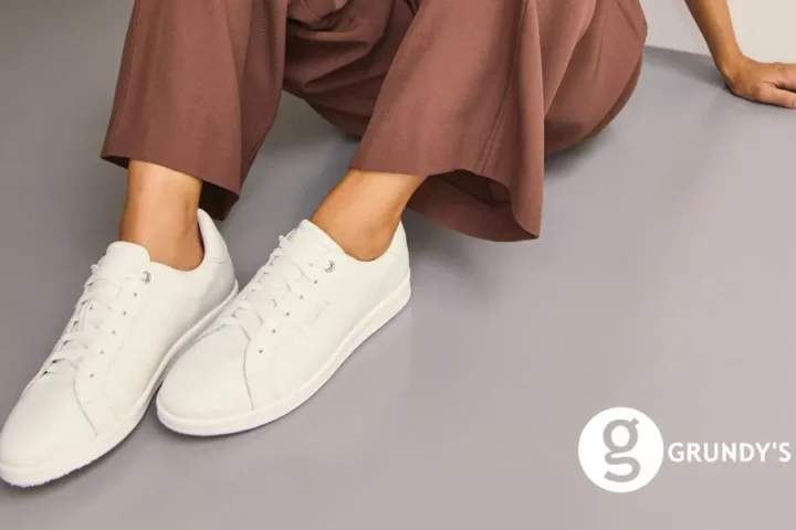 A woman's legs in white sneakers resting on a smooth gray floor.