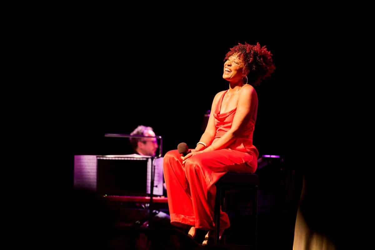 A woman in a red dress sits gracefully on a stool, exuding elegance and poise.