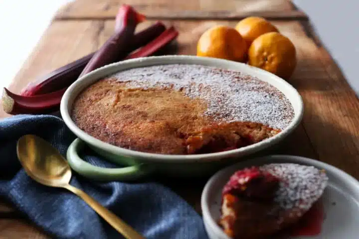 A bowl of pudding with a spoon beside it, accompanied by a colorful plate of assorted fresh fruit.