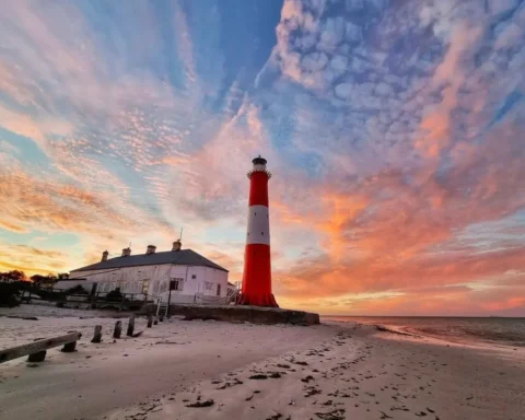 A lighthouse stands tall on a beach, silhouetted against a vibrant sunset sky.