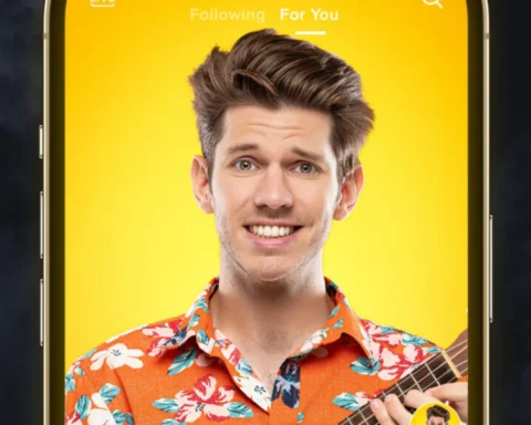 A man holding a guitar while looking at his phone, focused on the screen.
