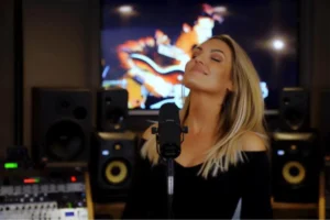 A woman passionately singing into a microphone in a professional recording studio, surrounded by sound equipment.