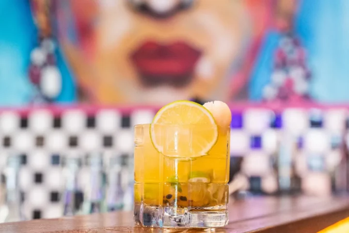 A refreshing drink garnished with a lemon slice sits on a wooden bar top.