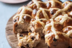 A hot cross bun with a slice taken out, revealing its soft, spiced interior and cross on top.