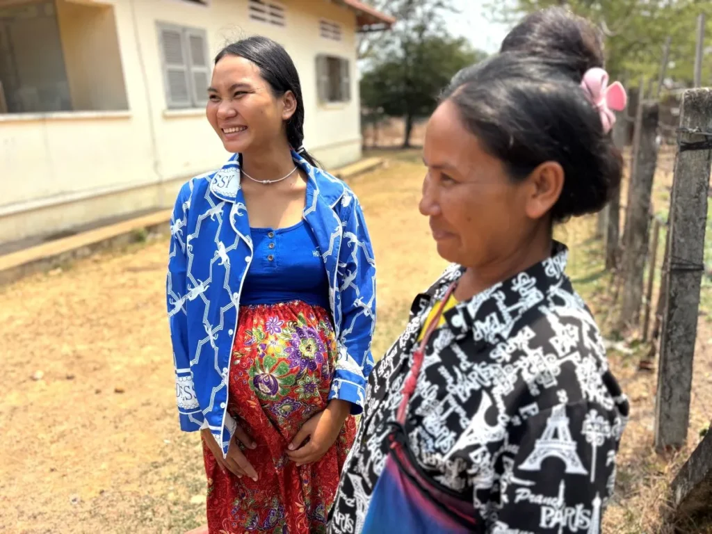 A smiling woman engages in conversation with another woman, both appearing friendly and animated.