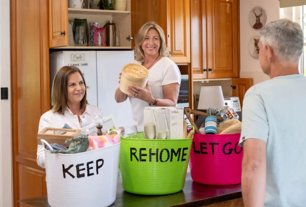 A woman and man stand in a kitchen with baskets labeled "keep home," "rehome," and "get go."