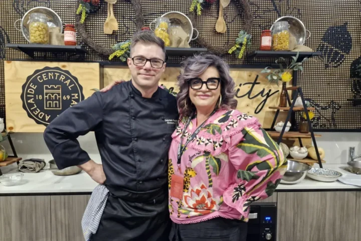 A man and woman stand together in a modern kitchen, smiling and looking at the camera.
