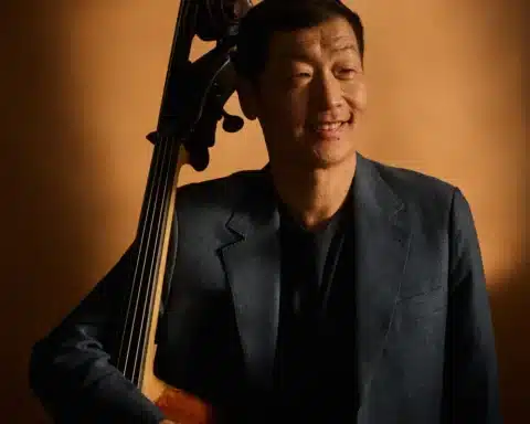 A man in a suit stands holding a cello, showcasing a blend of elegance and musical artistry.
