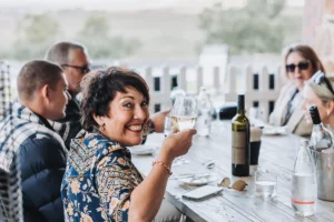 A woman raises a glass of wine in a toast at a restaurant table, smiling and enjoying the moment.