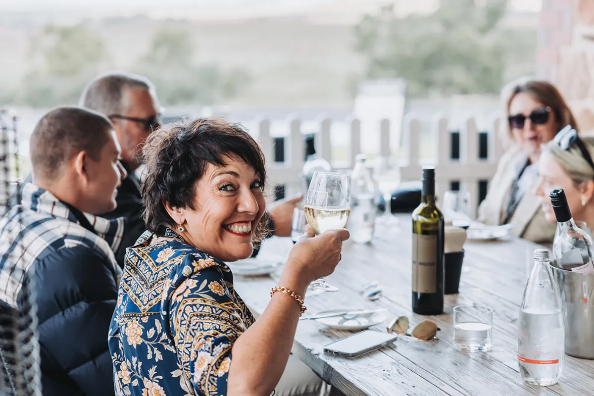 A woman raises a glass of wine in a toast at a restaurant table, smiling and enjoying the moment.