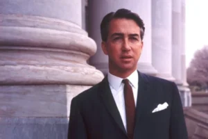 Don Dunstan in a suit and tie stands confidently in front of tall, classical pillars.