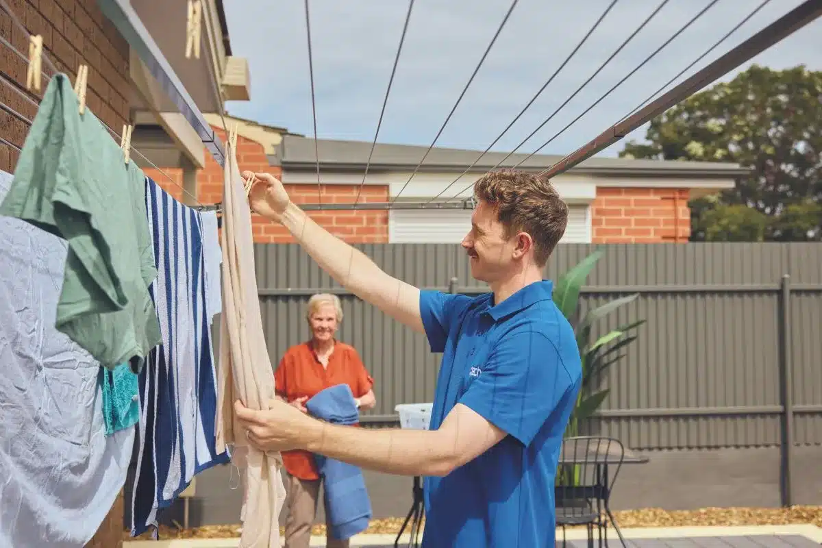 A man hangs freshly washed clothes on a clothesline under a clear blue sky.