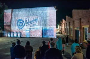 A group of people stands in front of a building displaying a colorful projection at night.