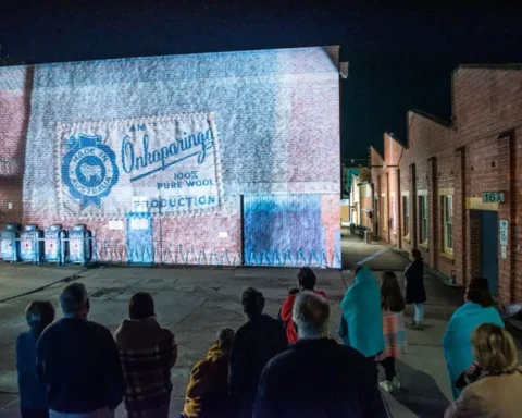 A group of people stands in front of a building displaying a colorful projection at night.