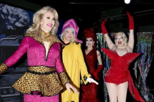 A group of women dressed in colorful costumes and elaborate makeup, smiling and posing together for the camera.