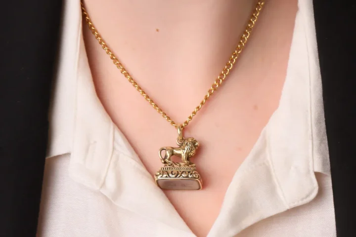 A woman wearing a gold necklace featuring a lion pendant.