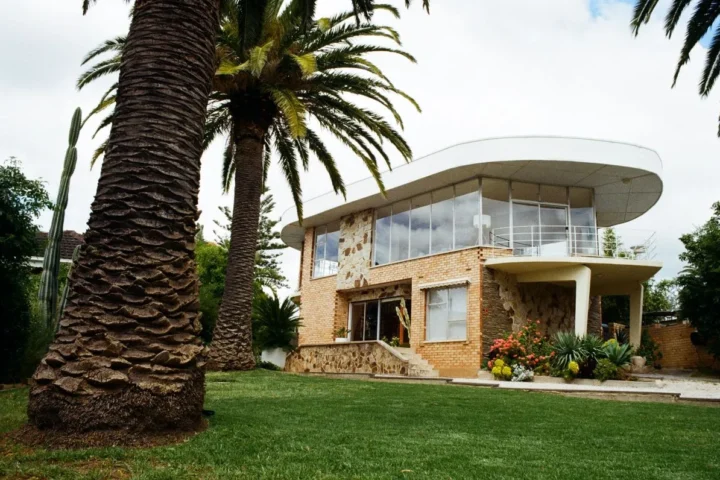 A modern house surrounded by a large lawn and palm trees, showcasing a bright and inviting outdoor space.