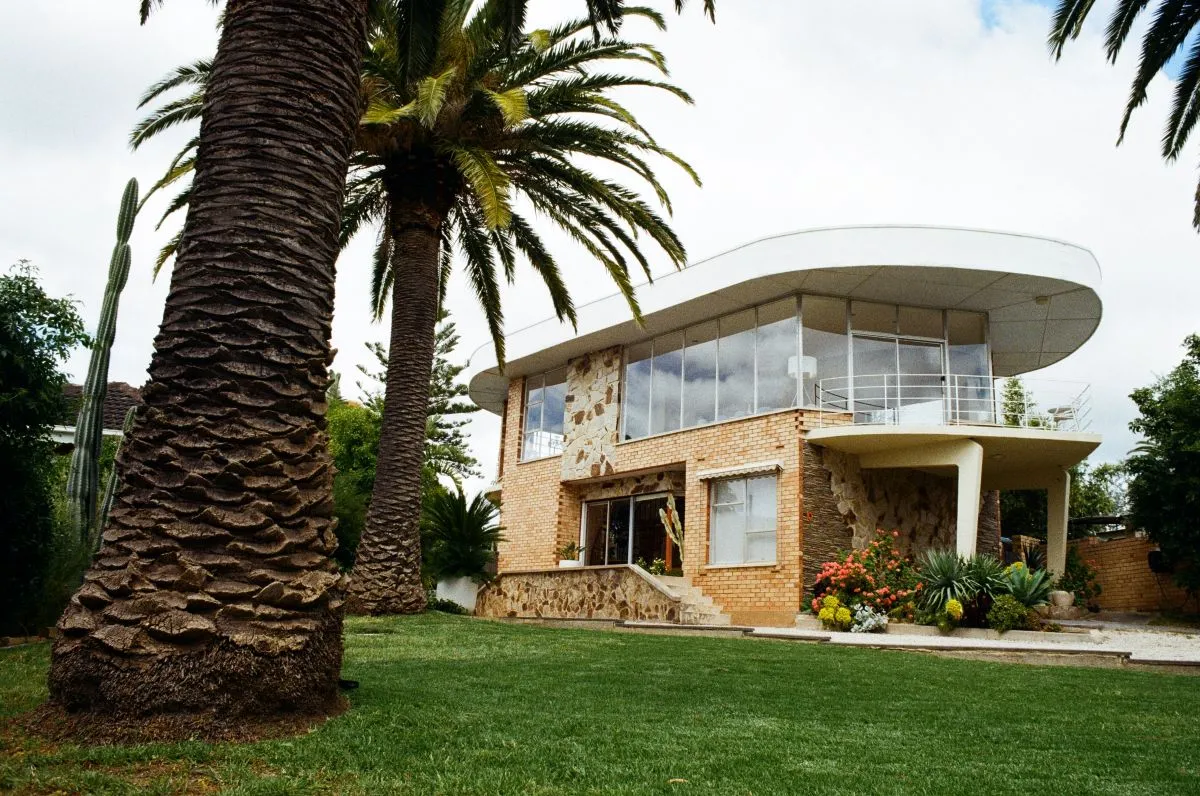 A modern house surrounded by a large lawn and palm trees, showcasing a bright and inviting outdoor space.