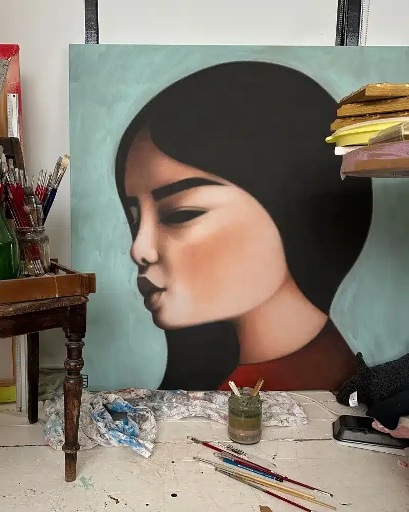 A painting of a woman's face hangs on the wall, showcasing her features and expression in vibrant colors.