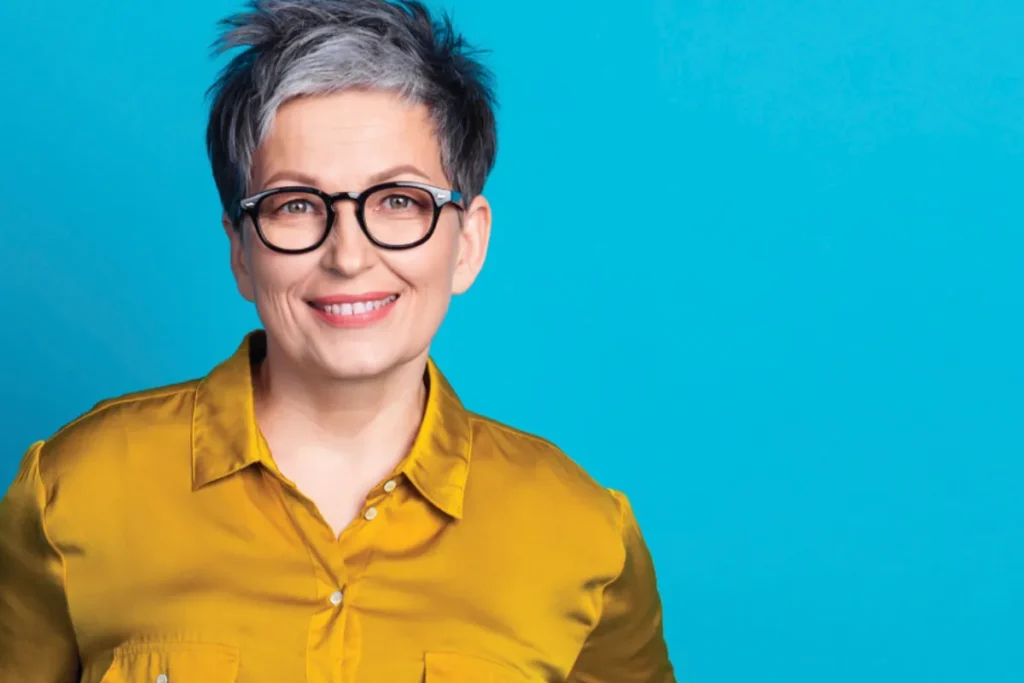 A woman wearing glasses and a bright yellow shirt smiles at the camera.