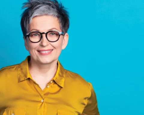 A woman wearing glasses and a bright yellow shirt smiles at the camera.