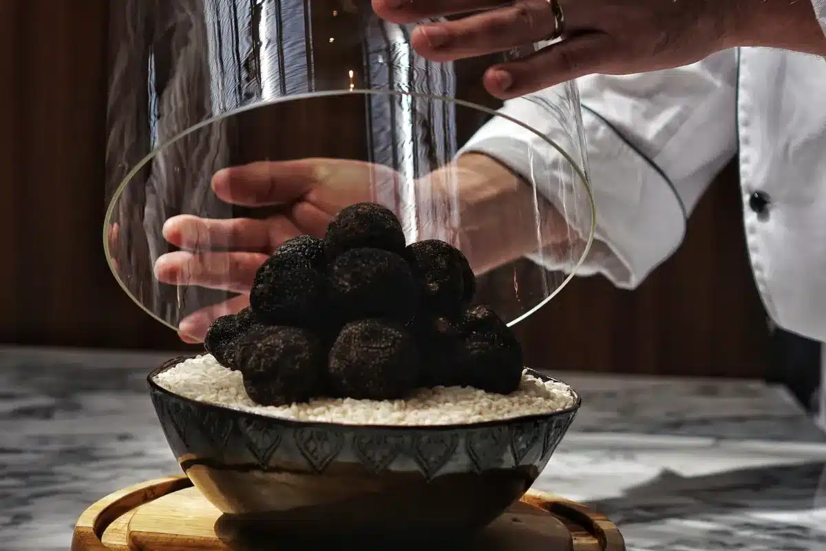 A chef pours black truffle balls from a bowl into a glass, showcasing a culinary preparation process.
