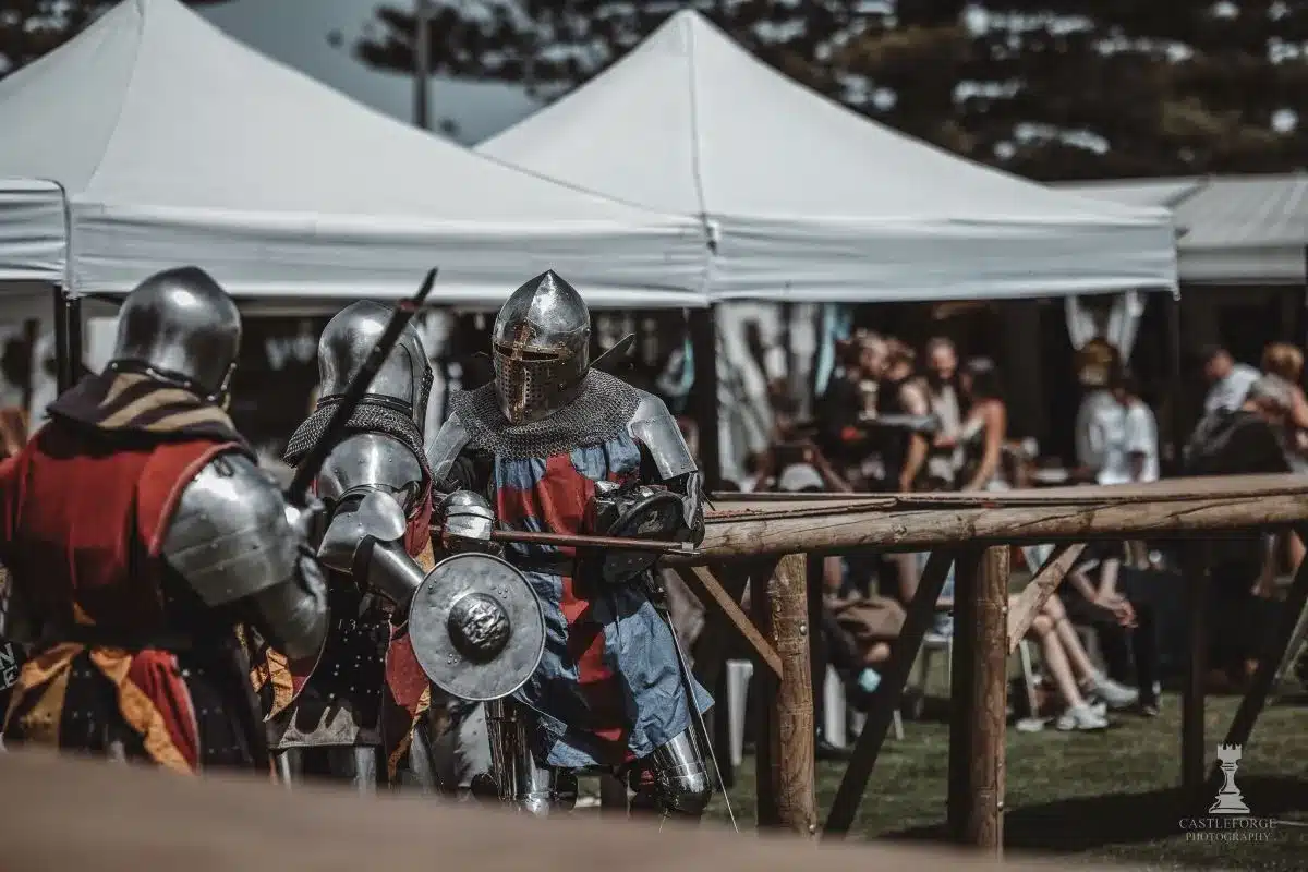 Two armored knights stand proudly in front of a colorful tent, ready for a medieval event or tournament.