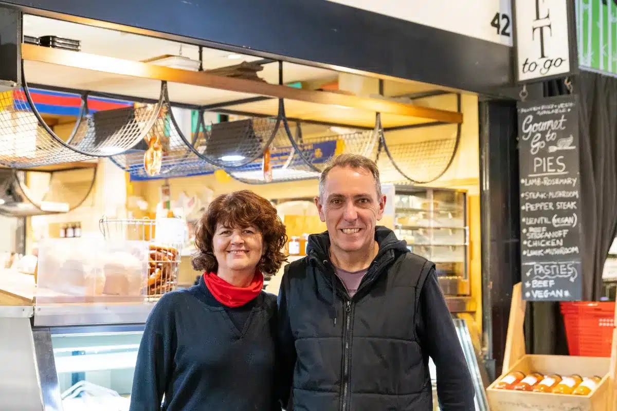 A man and woman stand together in front of a store, smiling and looking at the camera.