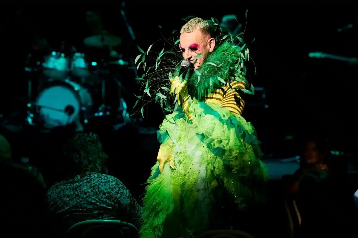 A person in a vibrant green feather costume passionately sings into a microphone on stage.
