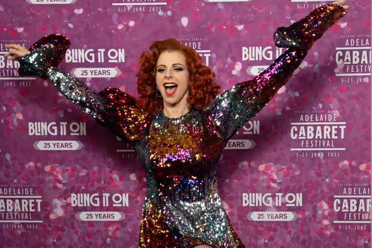 A woman with red hair wearing a sparkling sequin dress poses on a red carpet at a glamorous event.