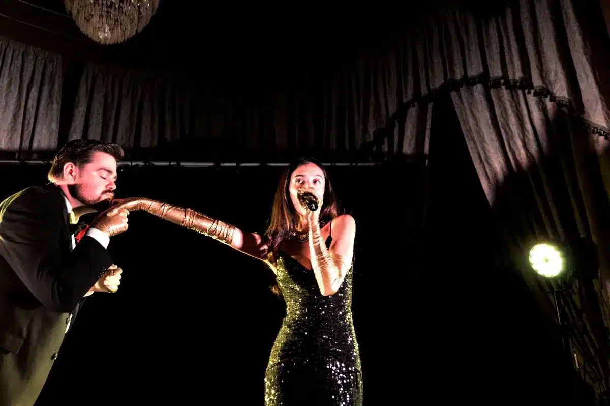 A man and woman in formal attire performing on stage, showcasing their talents to an engaged audience.