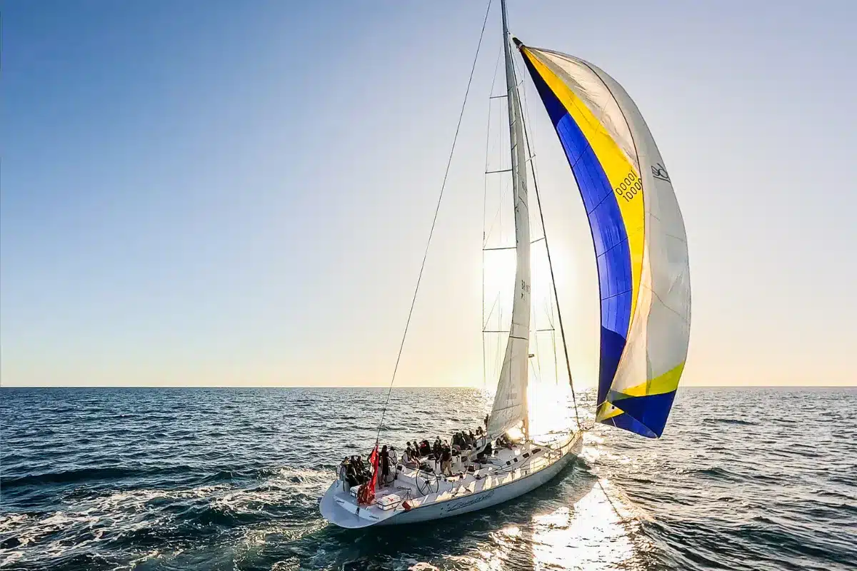 A sailboat with a vibrant yellow and blue sail gliding across the water under a clear sky.