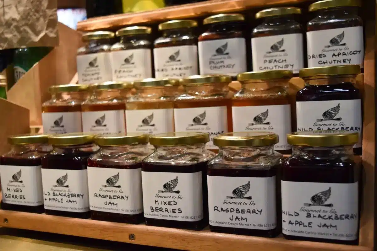 A colorful display of various jars filled with different types of jam on a wooden shelf.