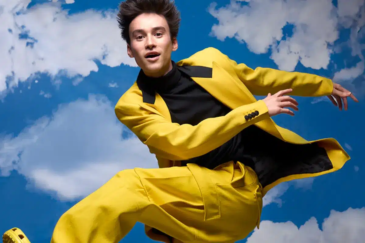A man wearing a bright yellow suit stands confidently, showcasing a bold fashion choice.