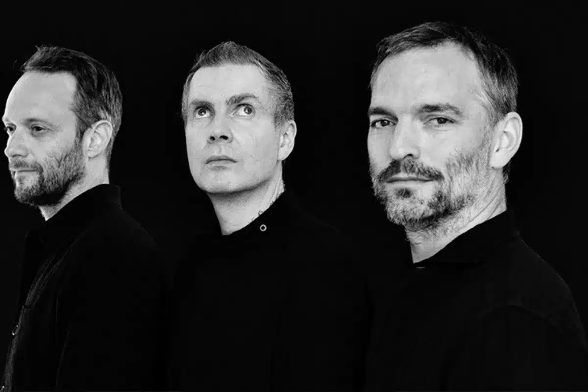 Three men in black shirts standing closely together, smiling at the camera.