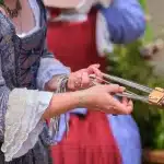 A woman in a renaissance dress holds a pair of scissors, poised as if ready to cut fabric or thread.
