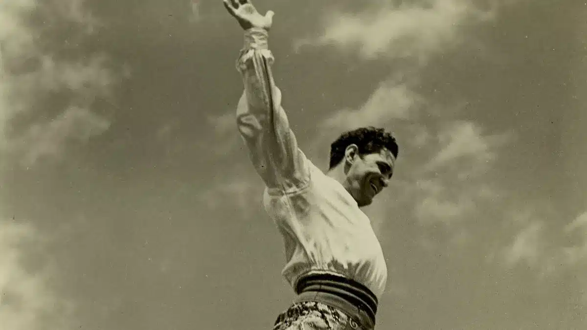 A man in a white shirt and pants is joyfully jumping against a clear blue sky.