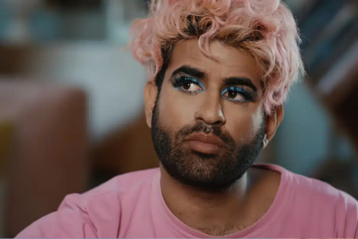 A man with vibrant pink hair and striking blue eyes gazes confidently at the camera.