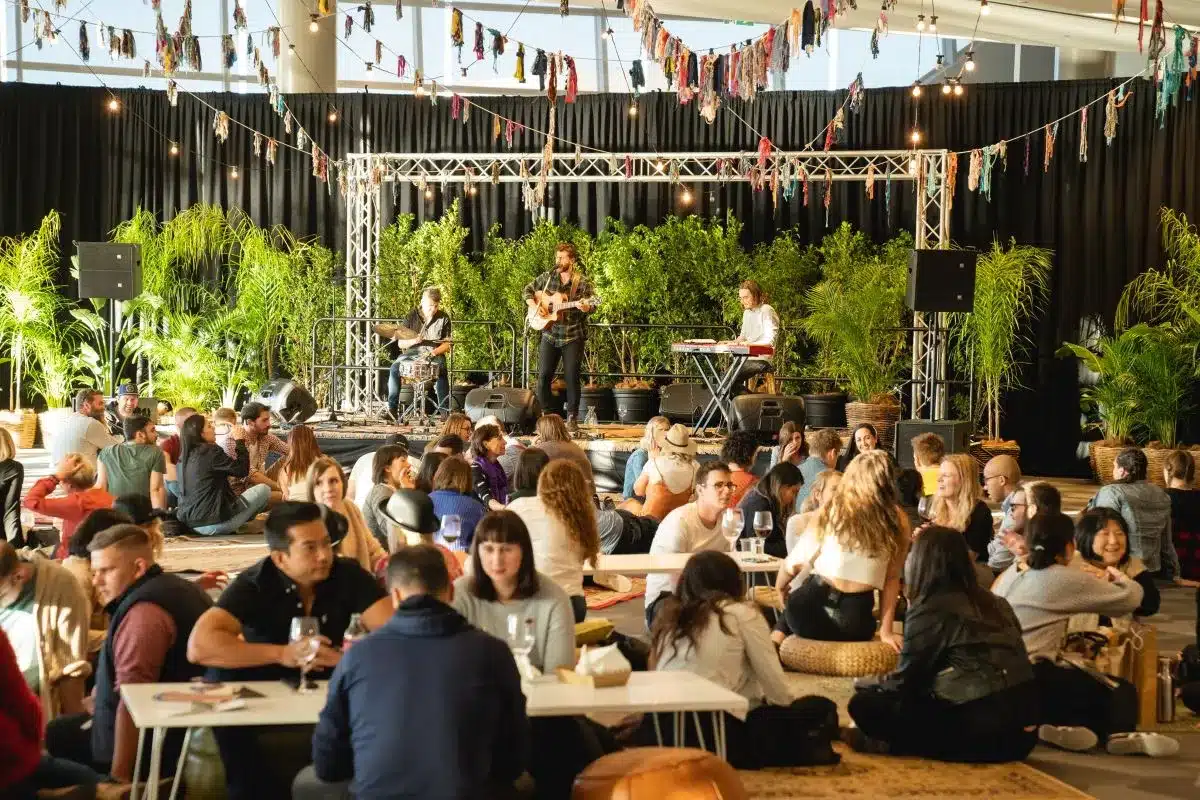 A large group of people seated at tables in a spacious indoor area, engaged in conversation and activities.