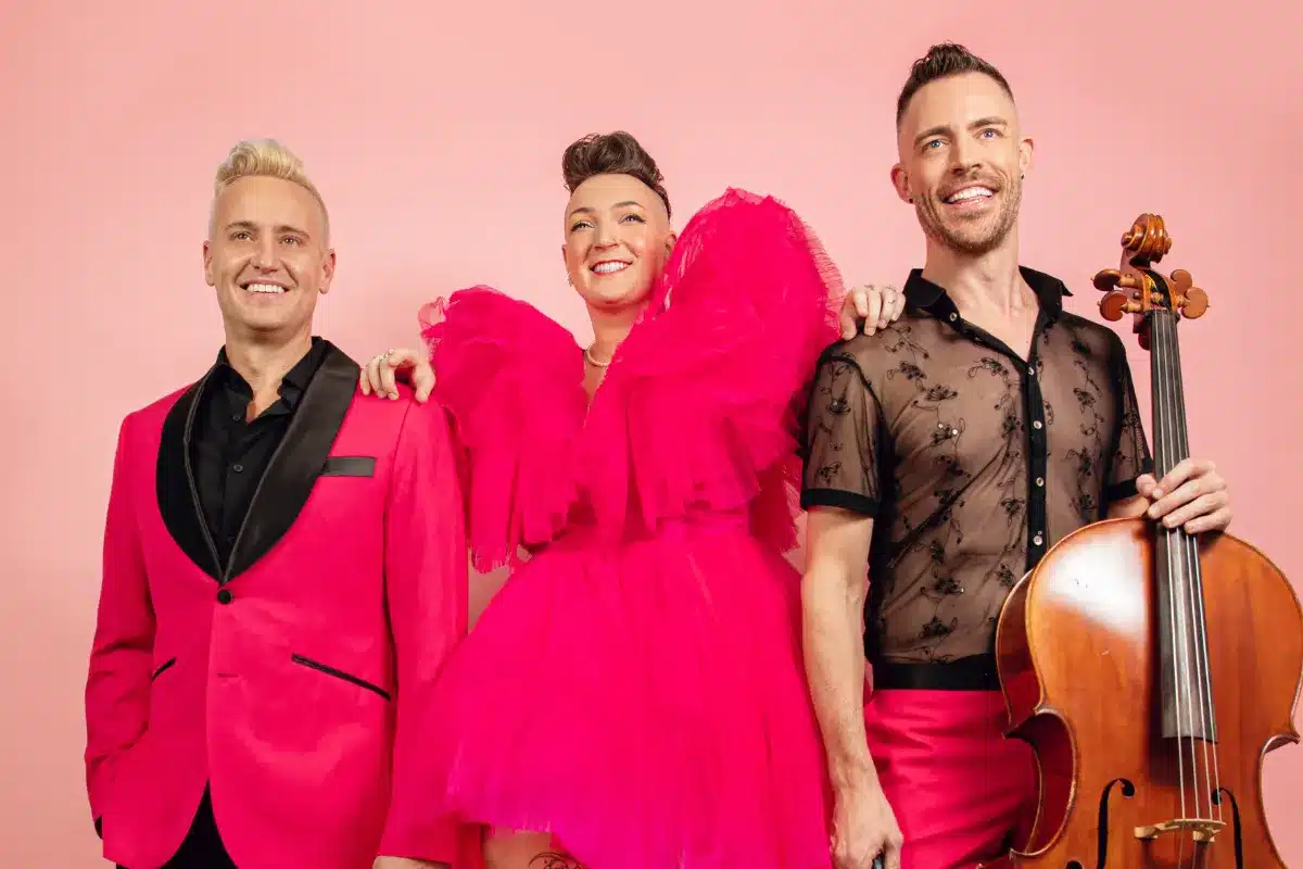 Three individuals in pink outfits smiling and posing together for a photo.