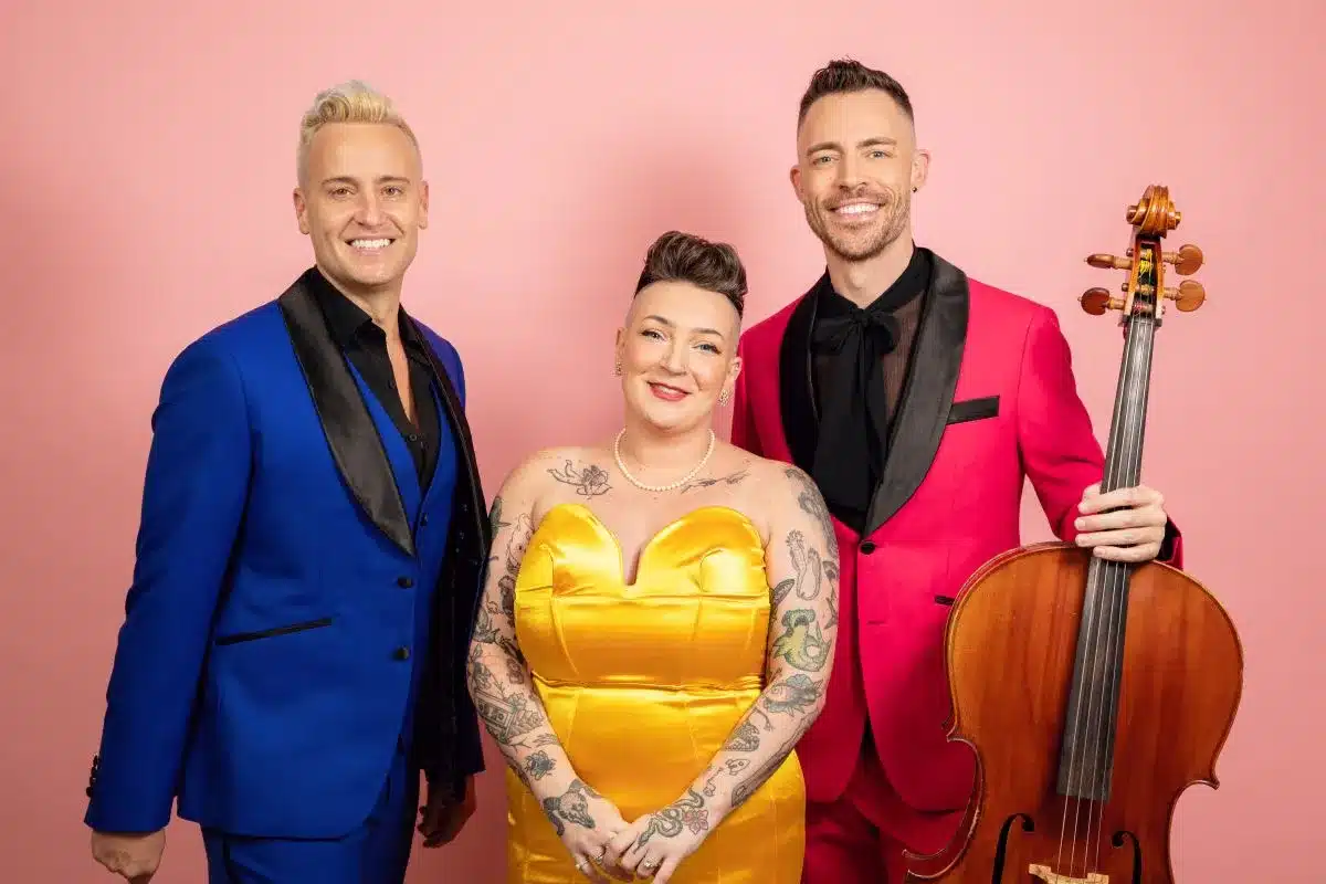 Three individuals in formal attire pose together for a photo, smiling and standing closely.