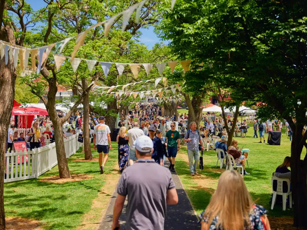 People stroll along a park path adorned with colorful bunting and flags, creating a festive atmosphere.