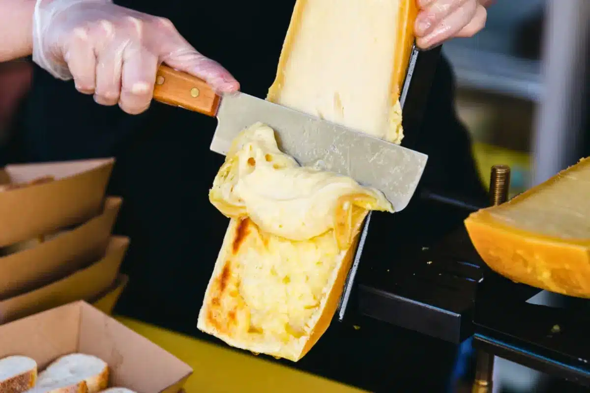 A person using a knife to cut a block of cheese on a wooden cutting board.