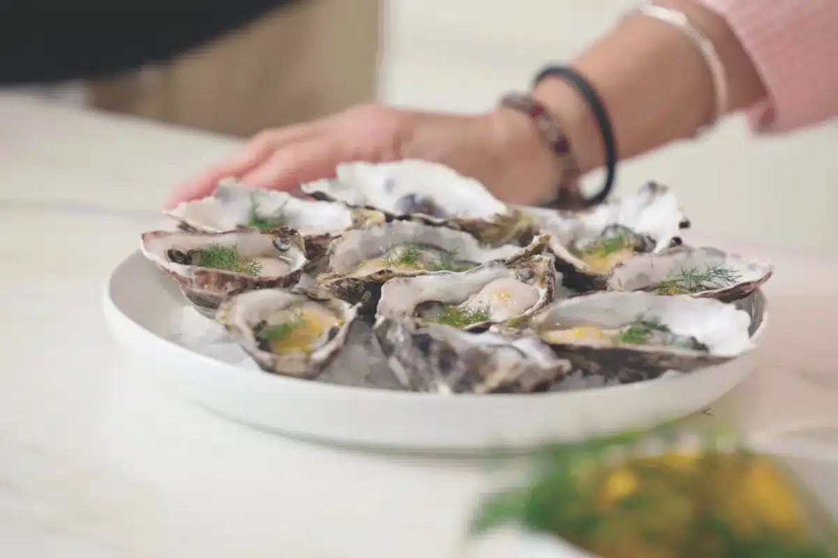 A woman holds a plate of oysters on a table, showcasing the seafood delicacy in an inviting setting.