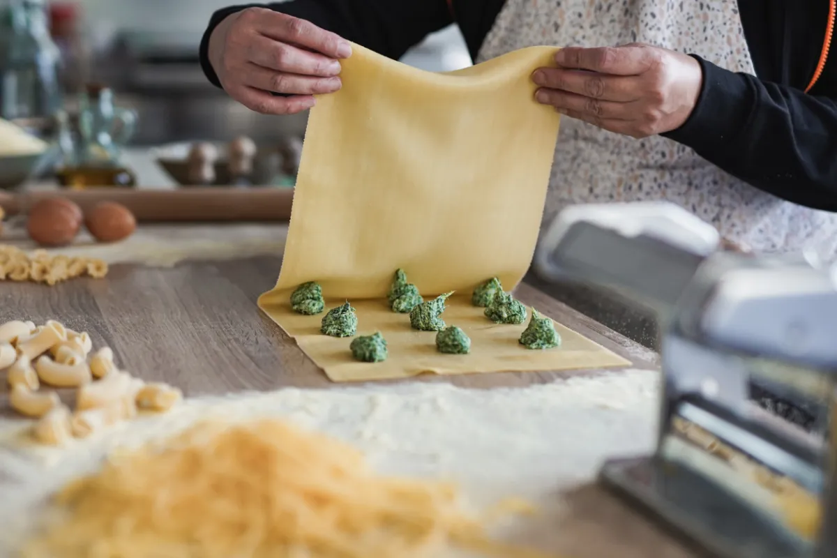  A person rolls out fresh pasta dough on a wooden table, using a rolling pin for an even thickness.
