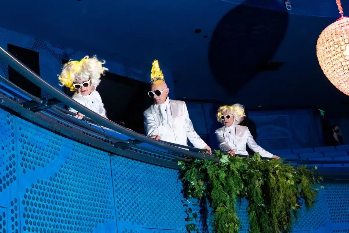 Three individuals in white suits and hats stand on a blue stage, presenting a unified and professional appearance.