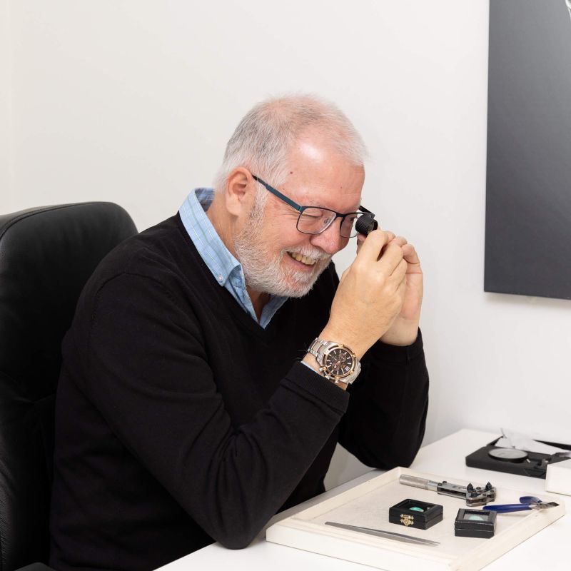  A man sitting at a desk, wearing a watch on his wrist, focused on his work.