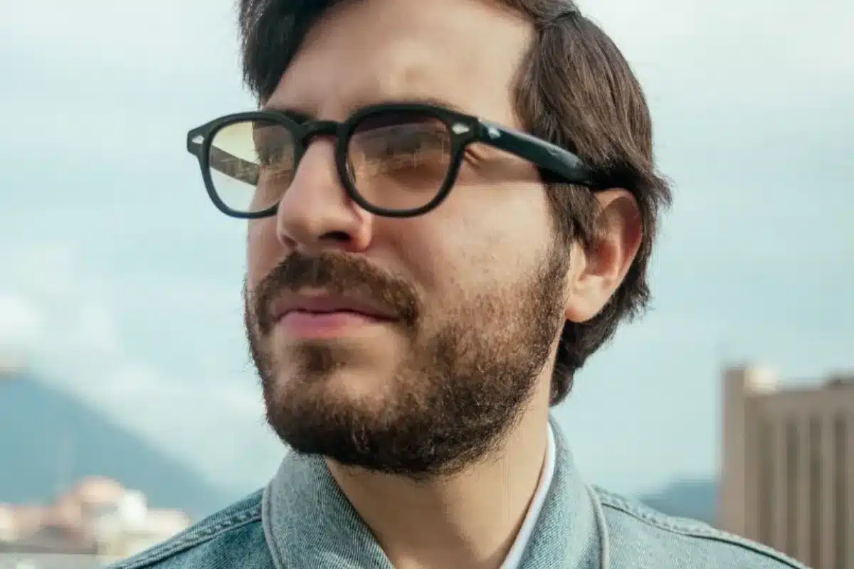 A man with glasses and a beard gazes thoughtfully to the side.
