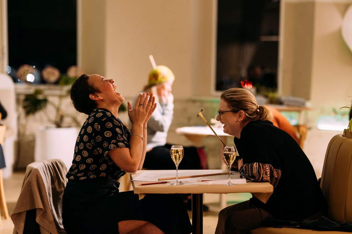 Two women seated at a table, enjoying wine together, with glasses raised in a toast.
