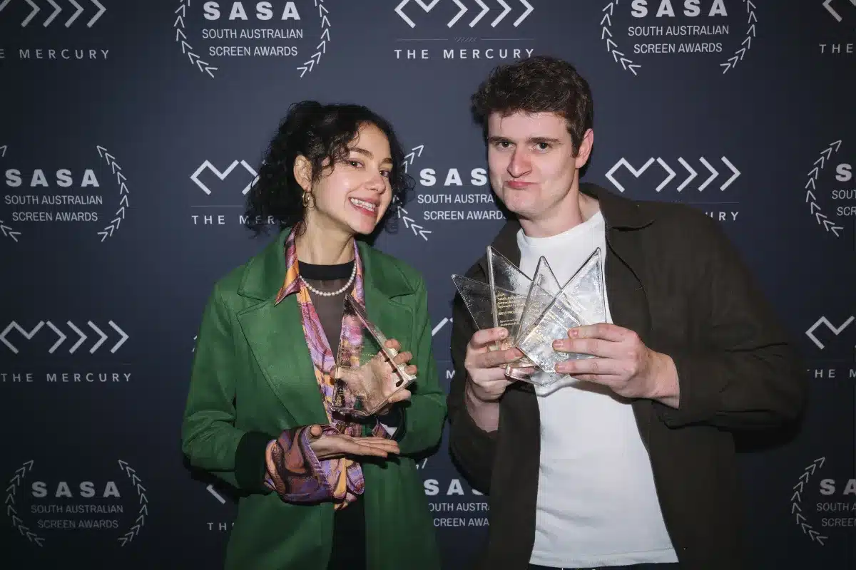 Two individuals proudly display their awards at a formal event, smiling and celebrating their achievements.